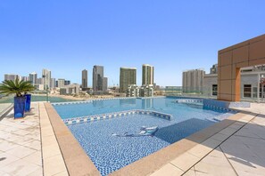 Una piscina en la azotea con vistas al horizonte urbano, suelo de baldosas y plantas en macetas.