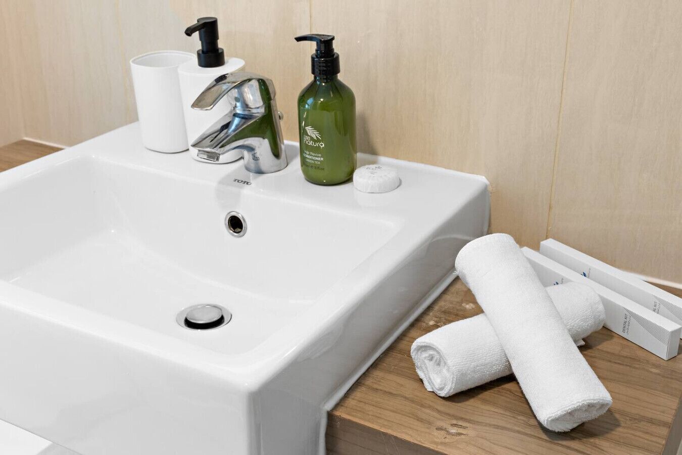 A white bathroom sink with a modern faucet, a green bottle of shampoo, and a white towel on the counter.
