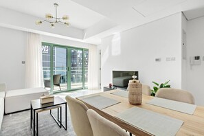 Uma sala de estar moderna com área de jantar, TV e uma janela grande com vista para um edifício.