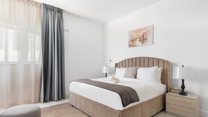 Une chambre d’hôtel moderne avec un grand lit, des tables de chevet, une chaise et un tableau au mur.