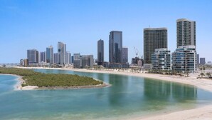 Un paysage urbain côtier avec des immeubles modernes de grande hauteur, une plage de sable et une étendue d’eau calme.