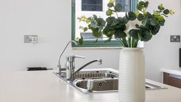 Una cocina moderna con un lavamanos de acero inoxidable, un jarrón blanco con follaje verde y una ventana con vistas al exterior.