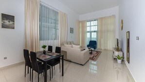 A modern living room with a dining area, a sofa, a blue armchair, and a TV. - Beachfront 1BR with Huge Balcony in Al Reem Island (Abu Dhabi)