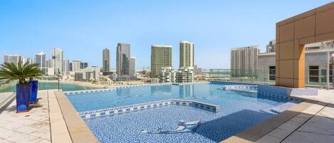 A rooftop swimming pool with a city skyline view, surrounded by buildings.