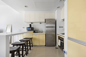 Una cocina compacta con refrigerador, microondas y estufa. Hay taburetes de bar y una pequeña mesa de comedor.