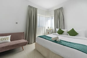Una habitación de hotel con cama, sofá, mesita de noche y cortinas.