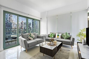 Een moderne woonkamer met twee grijze banken, een salontafel en een groot raam met uitzicht op de stad.