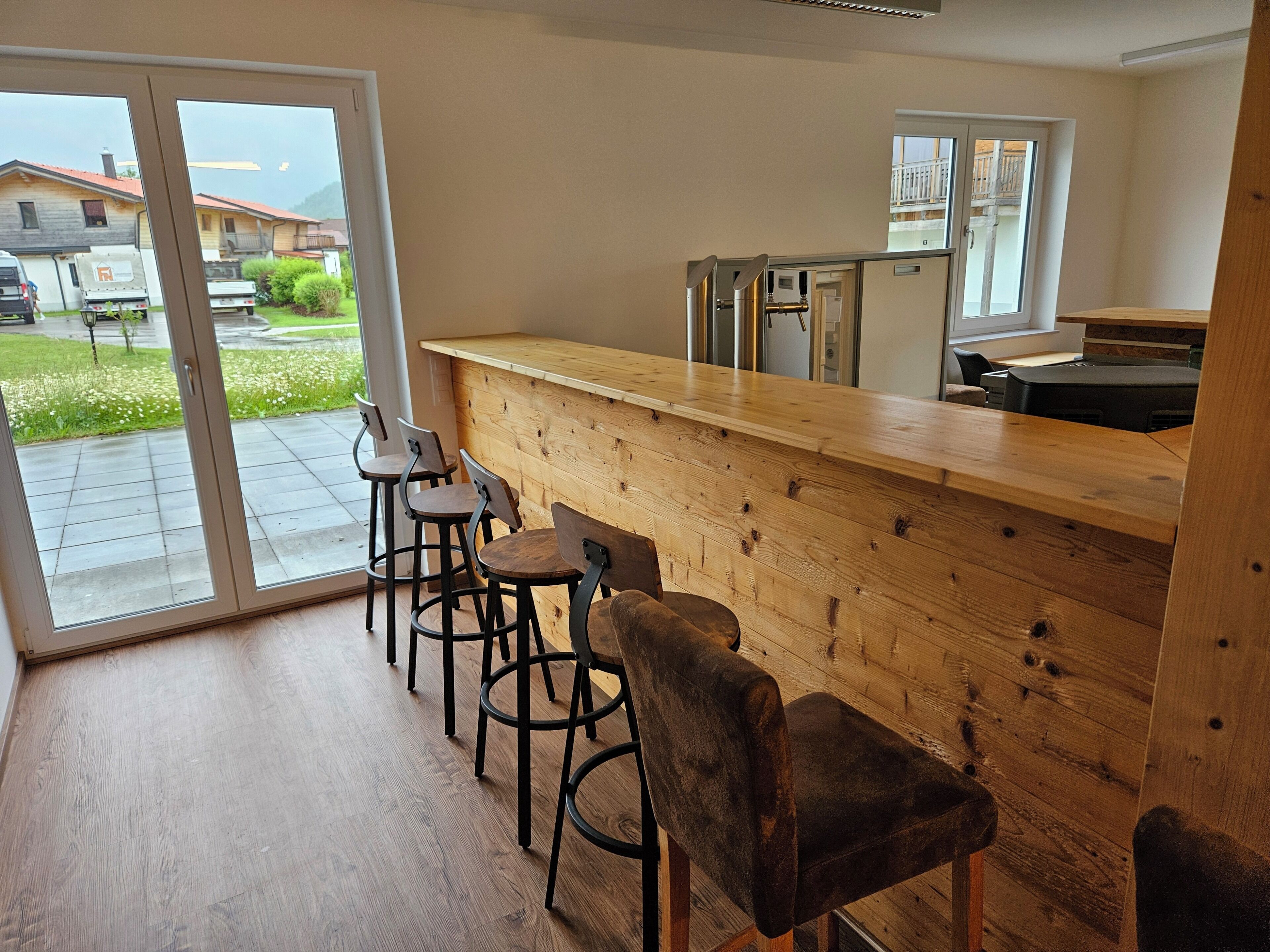 A bar area with wooden counter and stools, a sliding glass door leading outside, and a view of houses.