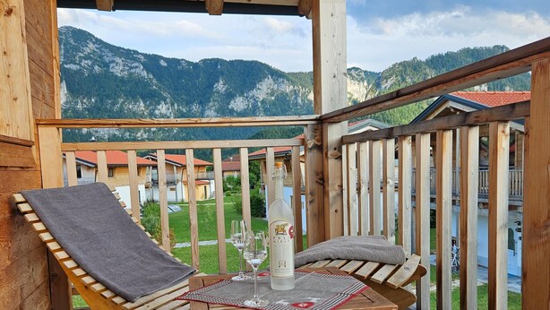 En træterrasse med hængekøjsstol og bord, med udsigt over et bjergrigt landskab.