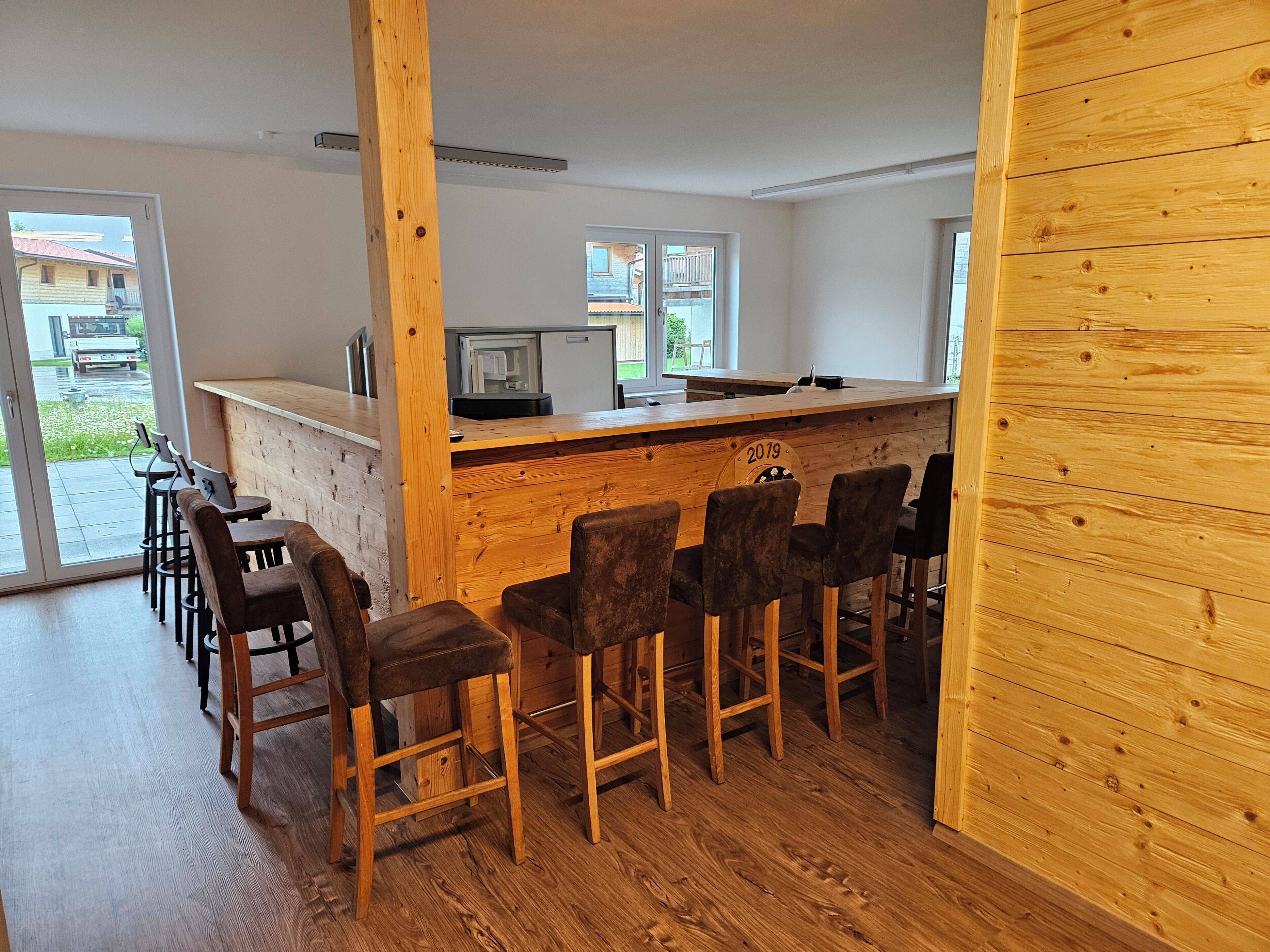 A bar area with wooden stools and a counter, a sliding glass door leading outside, and a view of a residential area.