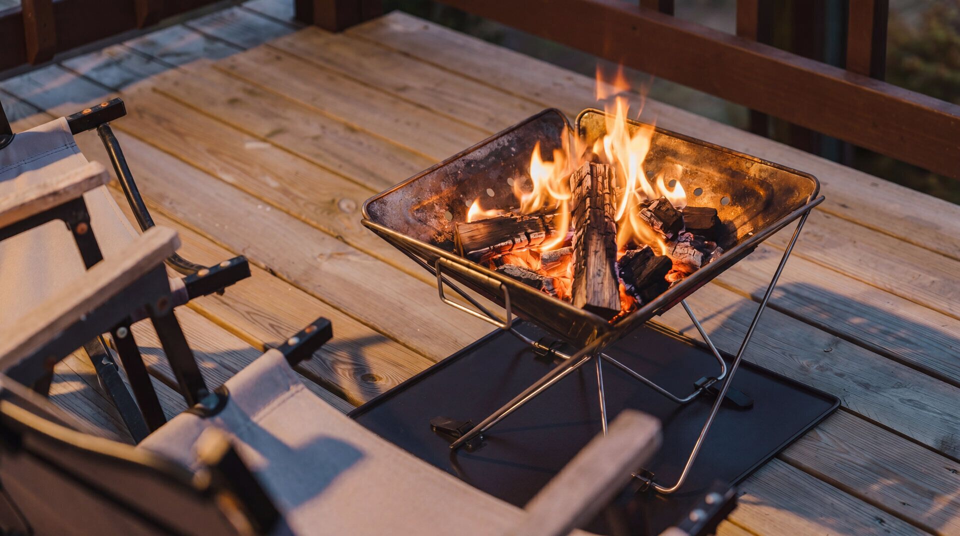 A metal fire pit with flames on a wooden deck.