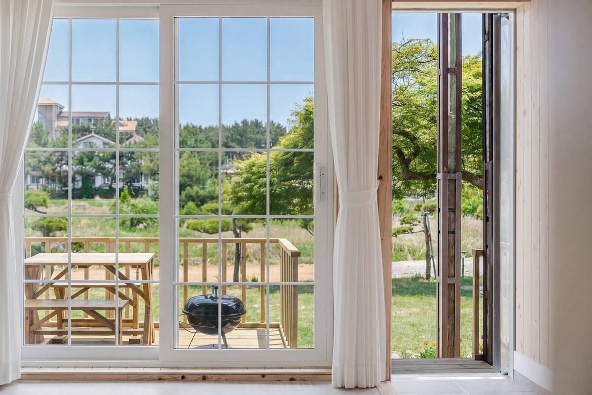 Una habitación con un amplio ventanal corredero que da a un patio exterior con mesa y parrilla de madera.