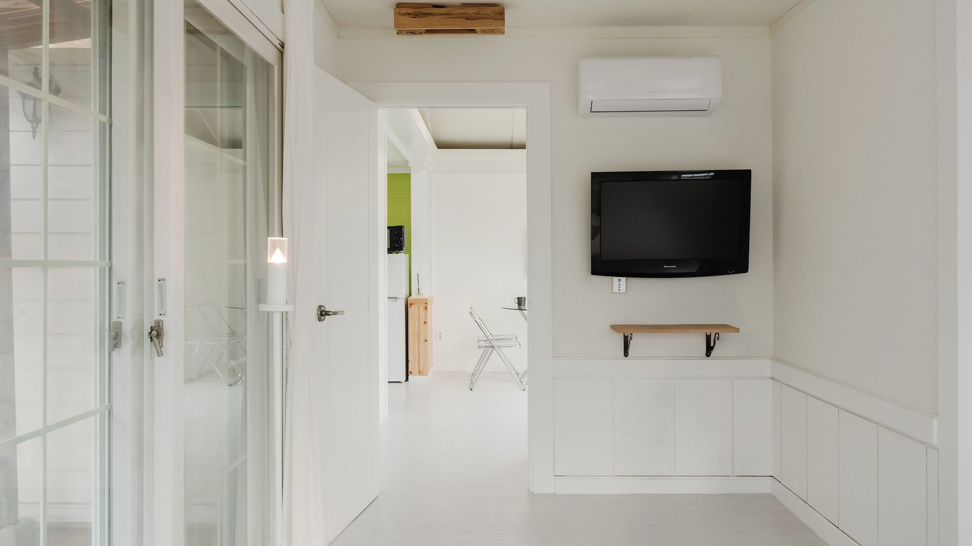 Un pasillo con puerta de cristal, un televisor montado y un pequeño estante de madera.