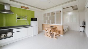 A compact kitchen with a green backsplash, white cabinetry, a wooden table, and a bed in the adjacent room.