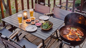 Una mesa de madera con una parrilla, platos, fuentes de comida y un farol.