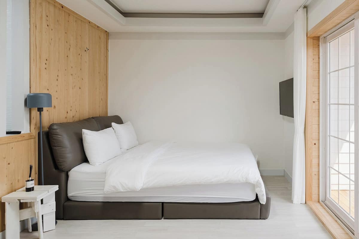 Un dormitorio moderno con cama, mesita de noche, lámpara y un amplio ventanal.