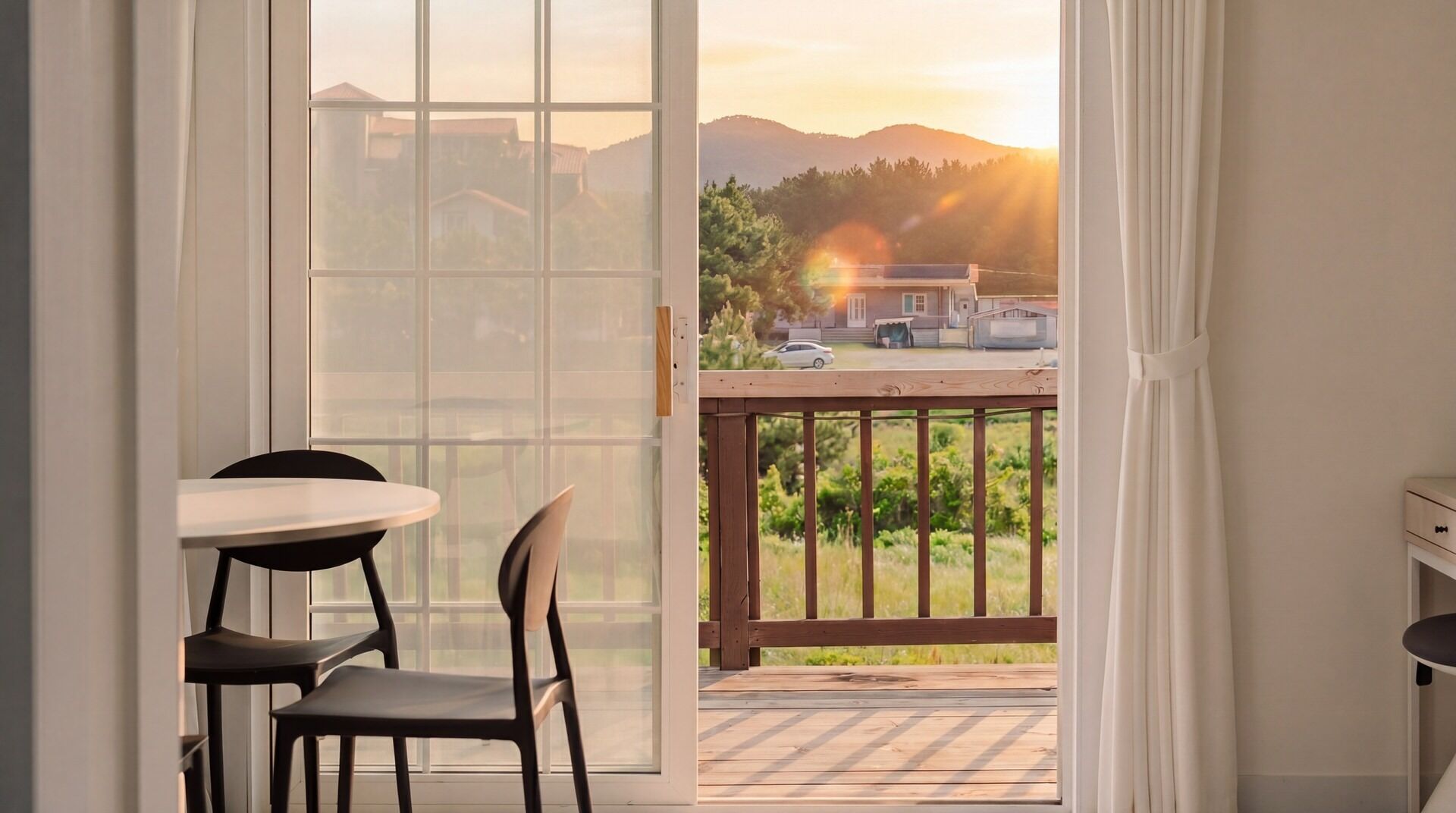 Una habitación con puerta de vidrio corrediza que da a un balcón con vistas a una casa y montañas.