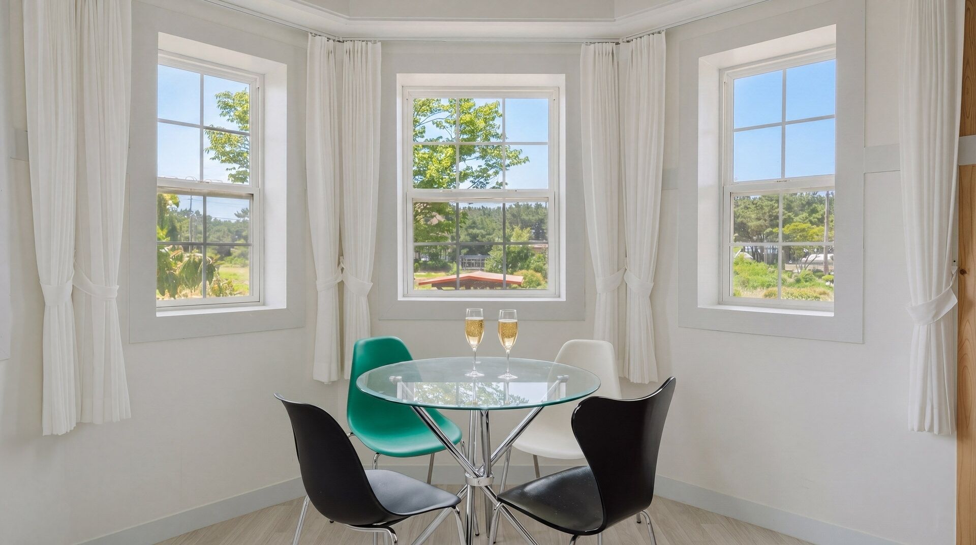 A corner room with a glass table, four chairs, and two champagne glasses.