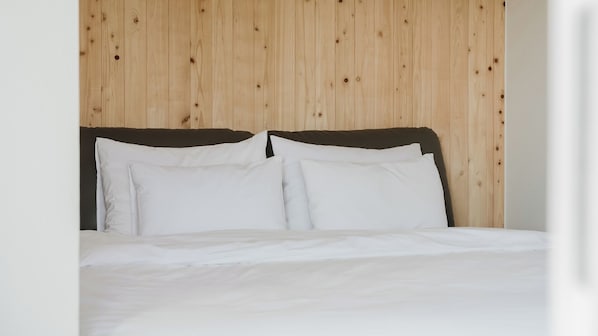 A bed with white bedding and a wooden headboard against a plain wall.