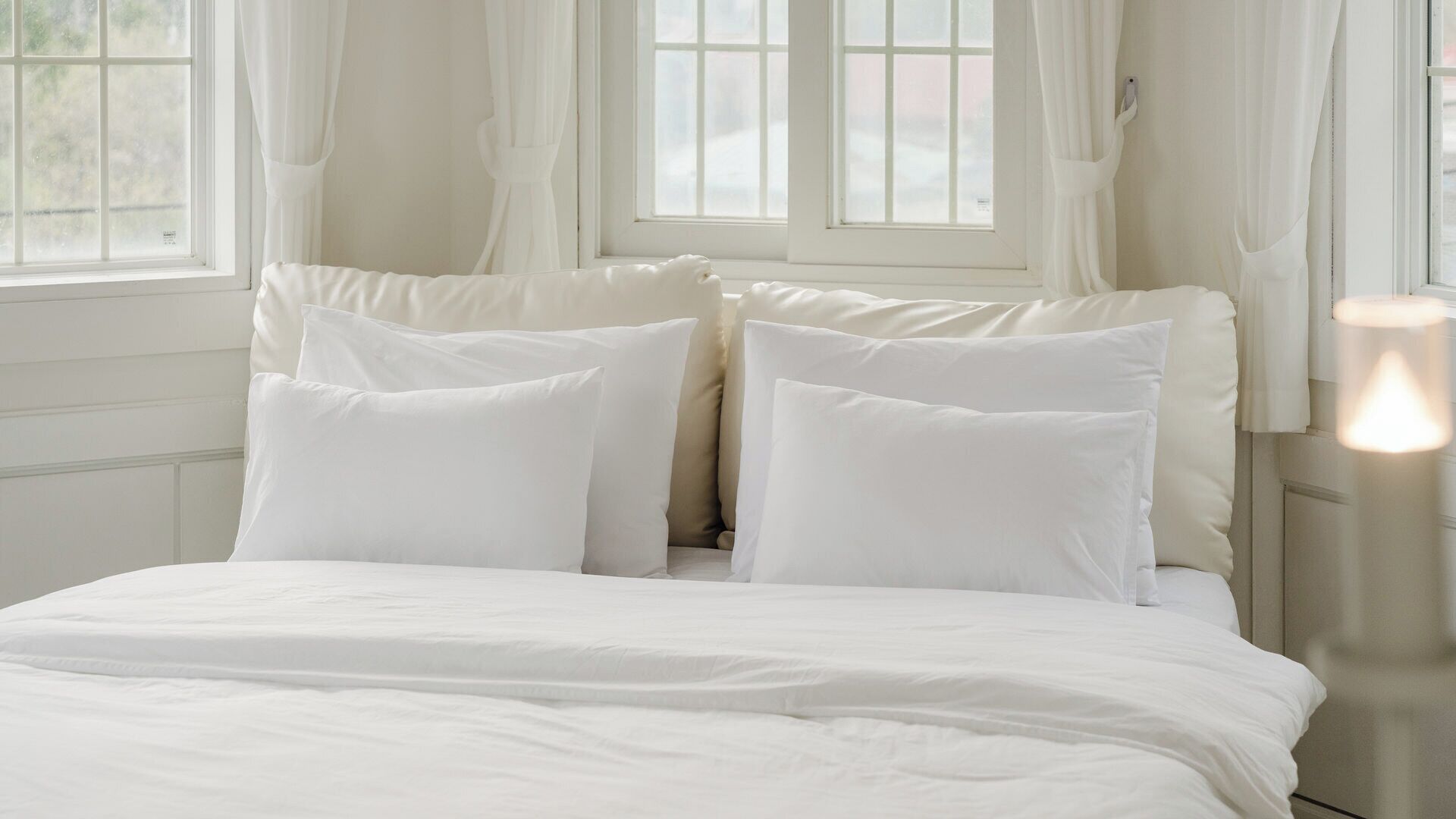 A bed with white bedding and pillows, a bedside lamp, and a window with curtains.