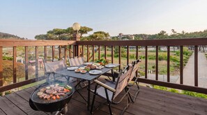 Eine Holzterrasse mit Esstisch, Grill und Blick auf einen Park.