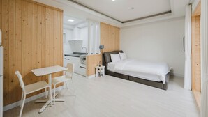 Ein Schlafzimmer mit Bett, kleinem Tisch, Stühlen, einer Küchenzeile und Holzvertäfelung.