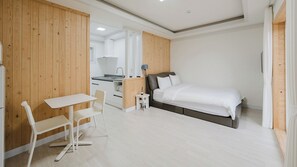 A bedroom with a bed, a small table, and chairs, a kitchenette, and wooden paneling.