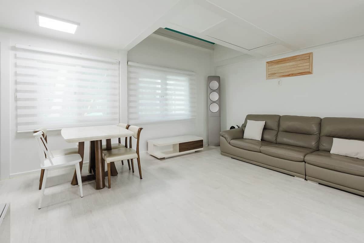 Una sala de estar moderna con un sofá, una mesa de comedor con sillas y un ventanal con persianas.