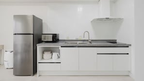 Una cocina moderna con un refrigerador de acero inoxidable, un microondas, un lavamanos y armarios blancos.