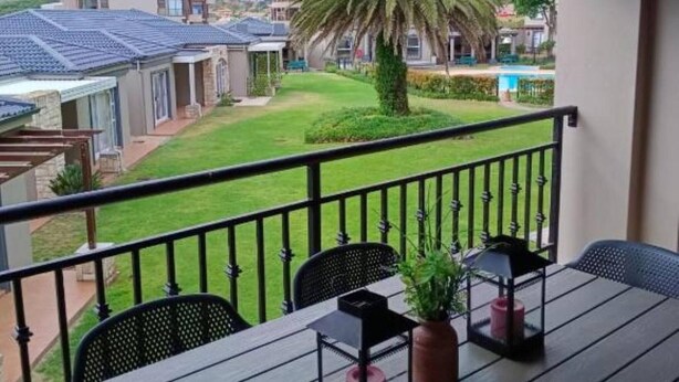 A balcony with a table, chairs, and a potted plant. - Secure 2-bedroom Apartment With Pool View in Mossel Bay (Mossel Bay)