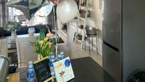 A kitchen area with a refrigerator, a water dispenser, a small table with a plant, and a sign that reads 'Veels Geluk Christmas.' - Secure 2-bedroom Apartment With Pool View in Mossel Bay (Mossel Bay)