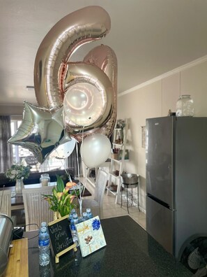A kitchen counter with a water bottle, a small plant, a gift box, and a sign that reads 'Veels Geluk Christmas.' - Secure 2-bedroom Apartment With Pool View in Mossel Bay (Mossel Bay)