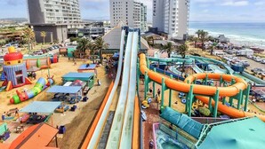 A water park with multiple slides and inflatable structures, a beach area with umbrellas, and a hotel in the background. - Secure 2-bedroom Apartment With Pool View in Mossel Bay (Mossel Bay)