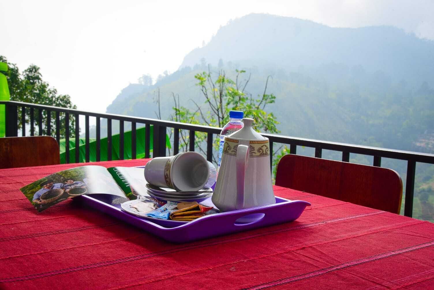 A table with a tray containing a water bottle, a teapot, and a magazine, set against a backdrop of a mountainous landscape.