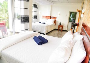Habitación de hotel con una cama grande, otra más pequeña, un balcón con una silla y zona de ducha.