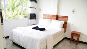A bedroom with a bed, a bedside table, a window with a view of palm trees, and a curtain. - Rokky Hill Cottage Ella (Ella)