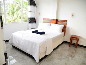A bedroom with a bed, a bedside table, a window with a view of palm trees, and a curtain. - Rokky Hill Cottage Ella (Ella)