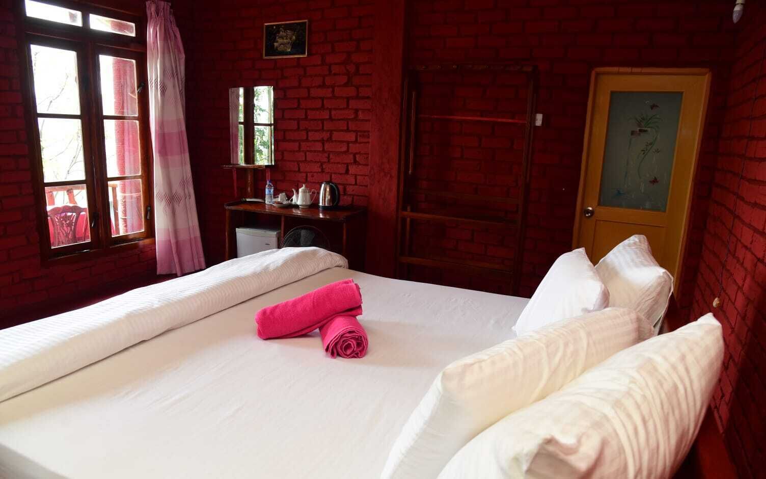 A hotel room with a large bed, a desk with a chair, a window with curtains, and a door with a picture.