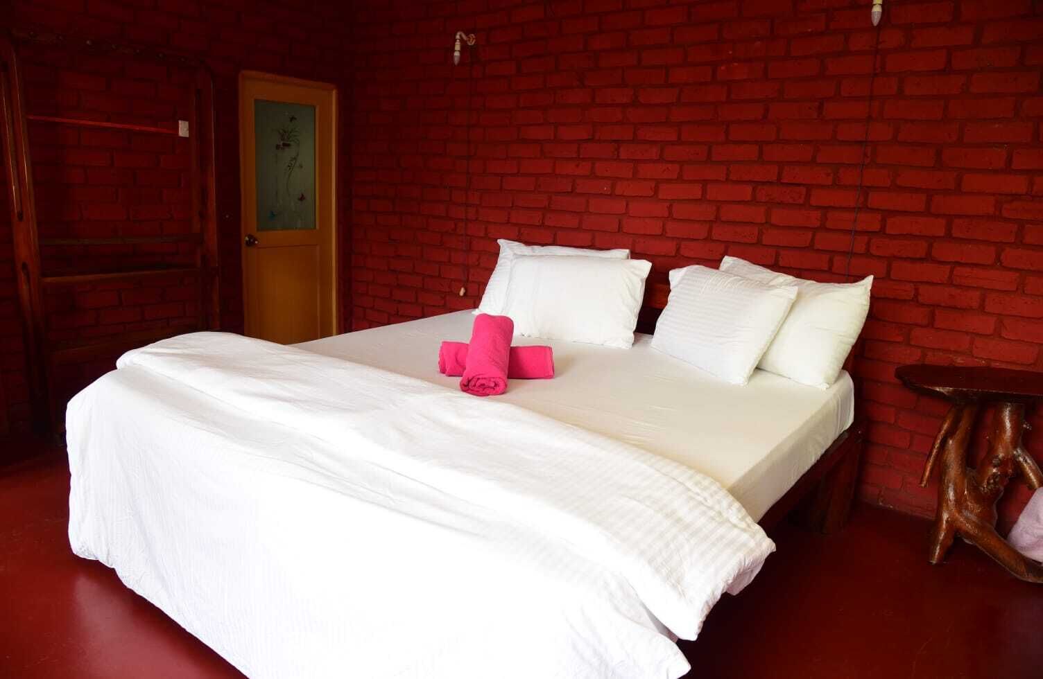 Una habitación de hotel con pared de ladrillo, una cama con ropa blanca, un cabecero de madera y una pequeña mesa de madera.