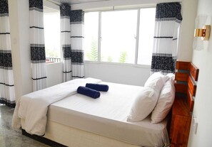 Una cama con ropa de cama blanca, dos toallas enrolladas y un cabecero de madera.
