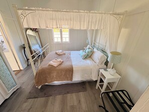 A bedroom with a four-poster bed, a bedside table with a lamp, and a chair.