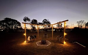 An outdoor seating area with a wooden pergola structure, chairs, and a fire pit.