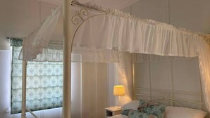 A four-poster canopy bed with a nightstand and lamp, a window with curtains, and a patterned wall.