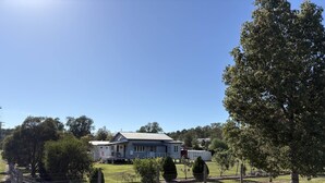 A two-story house with a porch, surrounded by a fenced yard with trees and a clear sky.