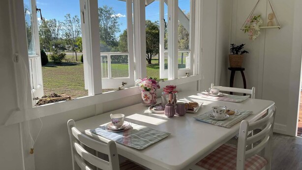 A white table with chairs, a window with a view of greenery, and a hanging plant.