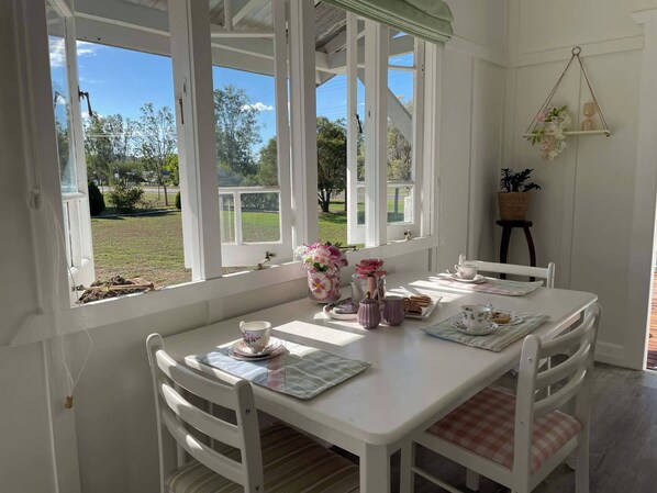 A white table with chairs, a window with a view of greenery, and a hanging plant.