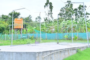A concrete platform with a metal structure, a water tank, and a green netted fence with vegetation.