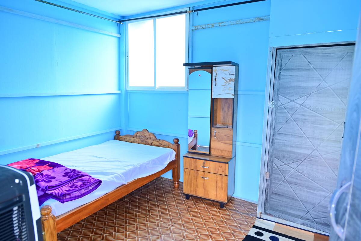 A room with a bed, a wooden dresser, a mirror, and a window.