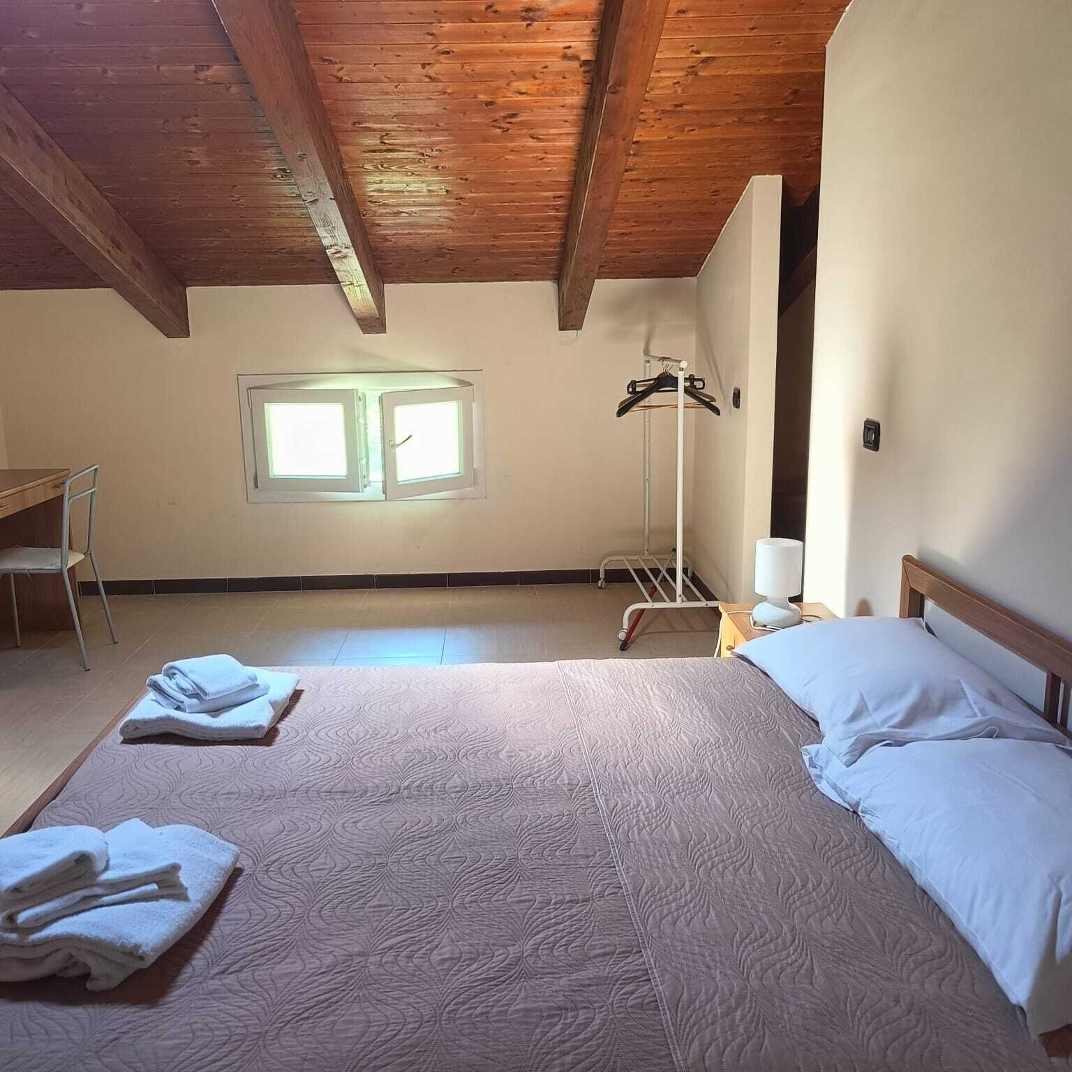 Un dormitorio con cama, una silla, un perchero y una ventana.