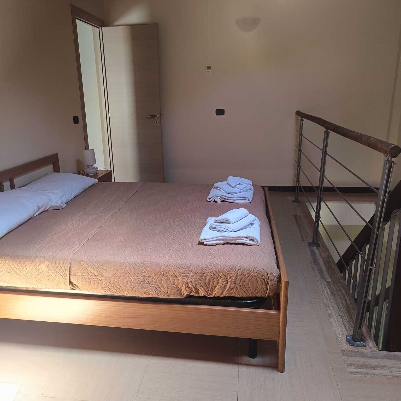 Una cama individual con estructura de madera, colchón marrón y dos toallas blancas dobladas en el reposapiés.